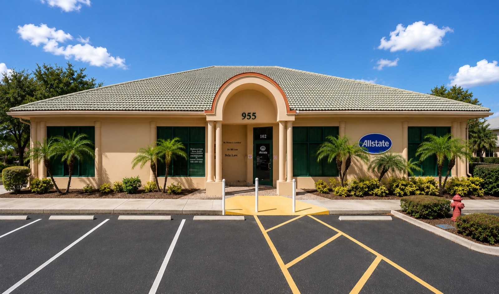955 East Del Webb Boulevard: a single-story tan stucco office building with a green tile roof, a barrel-vaulted columned entry and palms along the front.