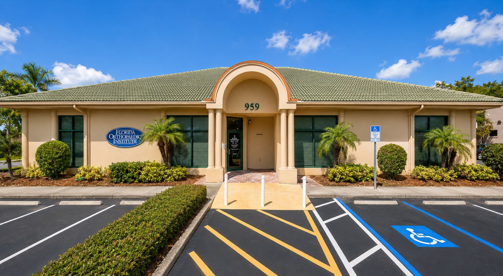 959 East Del Webb Boulevard: a single-story tan stucco office building with a green tile roof and barrel-vaulted columned entry, matching its neighbors at 955 and 957.