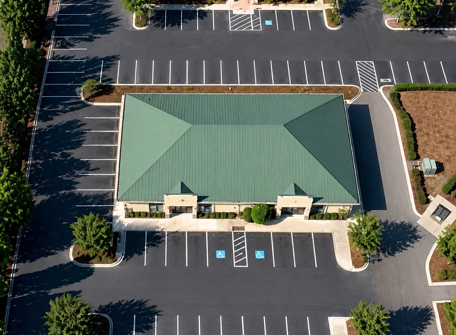Aerial view of Sun Plaza Building 4: a single-story building with a green standing-seam metal roof and two gabled entry porticos, surrounded by open parking.